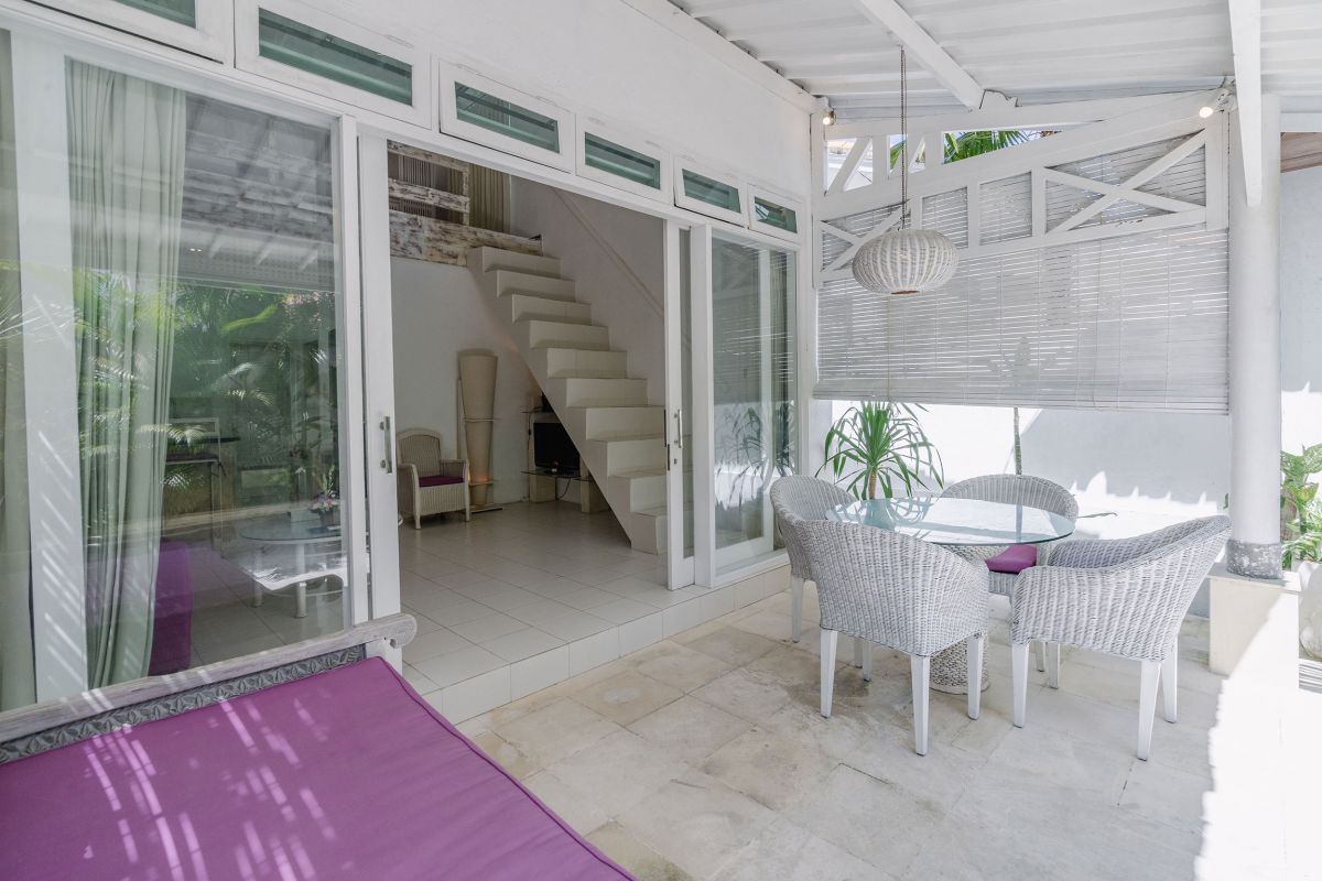 Modern minimalist living room interior with white wooden staircase, bar counter with purple stools, floral coffee table, and neutral decor. - Bali Villas
