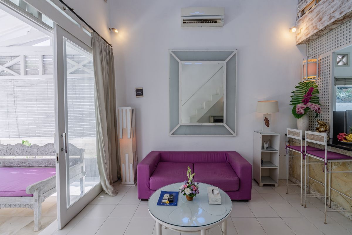 Modern minimalist living room interior with white wooden staircase, bar counter with purple stools, floral coffee table, and neutral decor. - Bali Villas