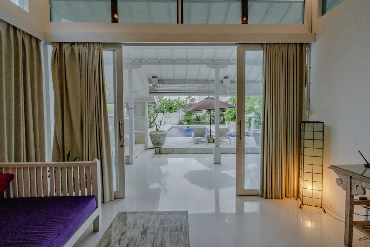 Spacious Balinese loft living room with wooden mezzanine stairs, purple sofa, TV console, white coffee table, and tropical wall art. - Bali Villas