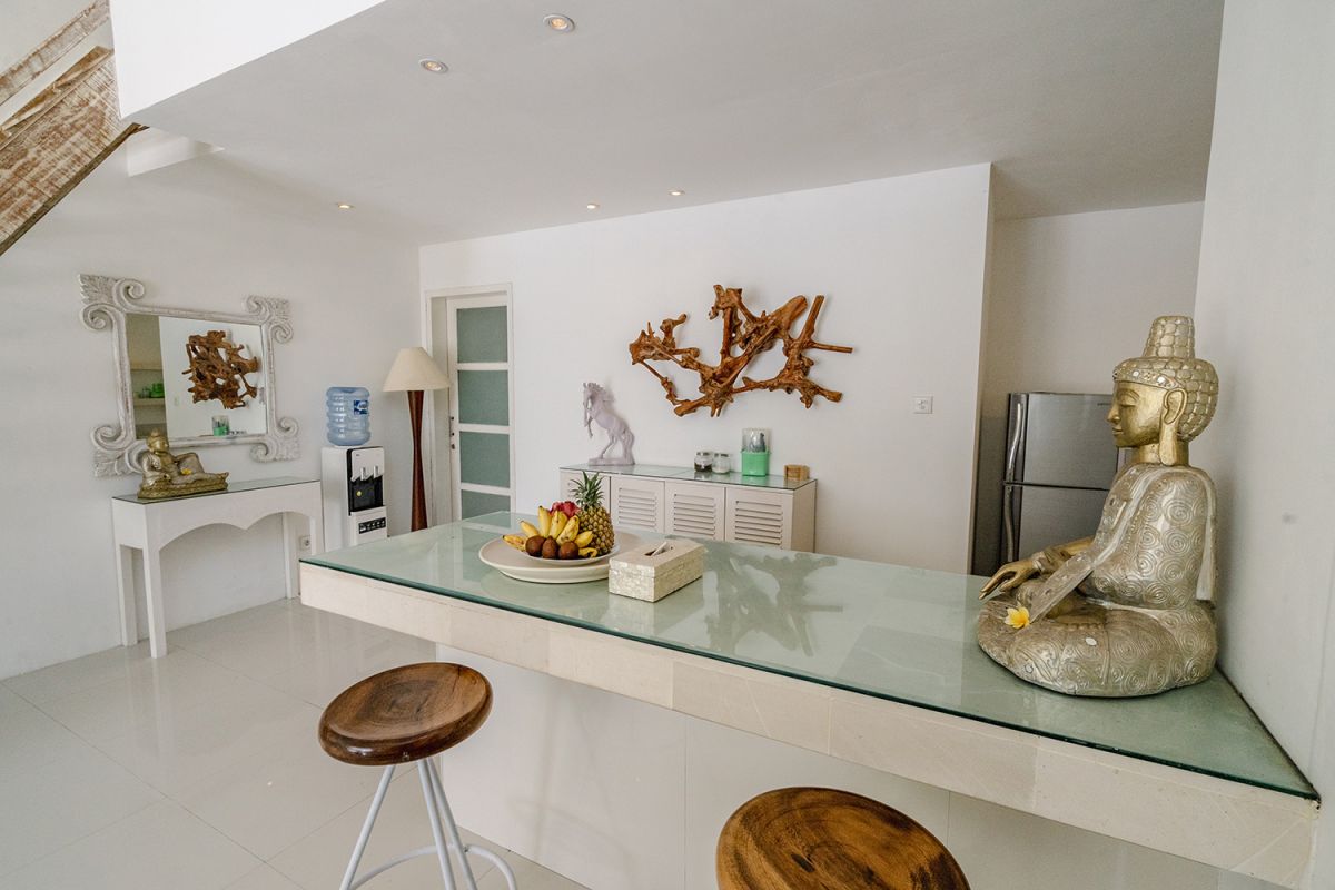 Spacious Balinese loft living room with wooden mezzanine stairs, purple sofa, TV console, white coffee table, and tropical wall art. - Bali Villas