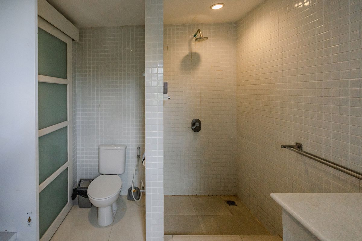 Spacious Balinese loft living room with wooden mezzanine stairs, purple sofa, TV console, white coffee table, and tropical wall art. - Bali Villas