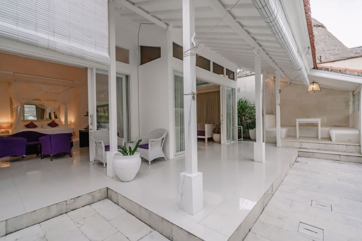 Spacious Balinese loft living room with wooden mezzanine stairs, purple sofa, TV console, white coffee table, and tropical wall art. - Bali Villas