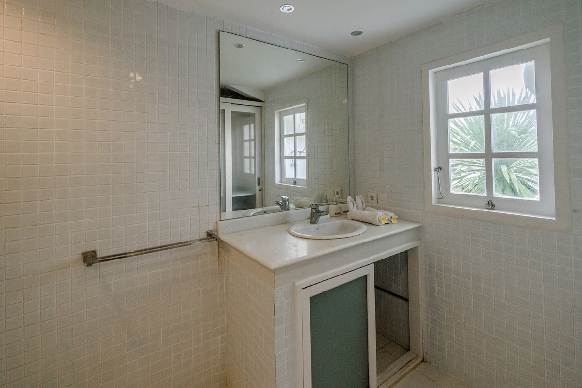Spacious Balinese loft living room with wooden mezzanine stairs, purple sofa, TV console, white coffee table, and tropical wall art. - Bali Villas