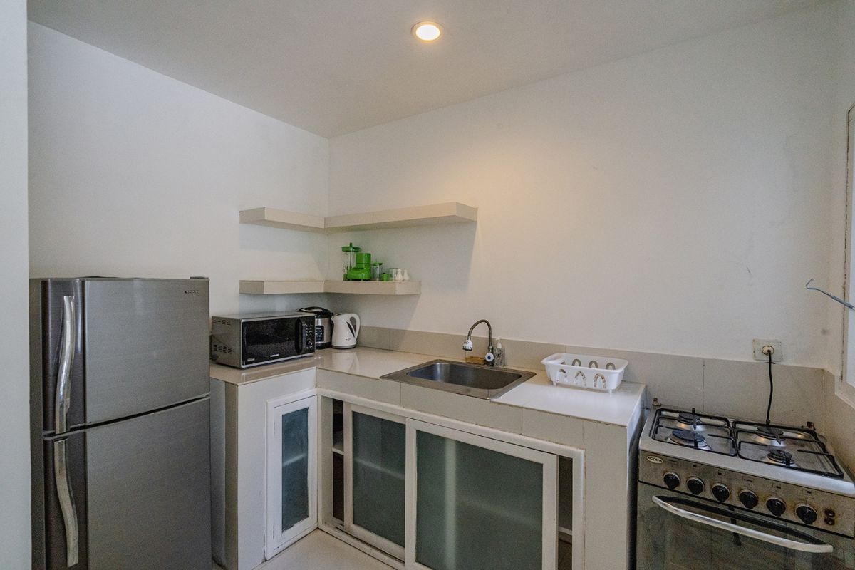 Spacious Balinese loft living room with wooden mezzanine stairs, purple sofa, TV console, white coffee table, and tropical wall art. - Bali Villas