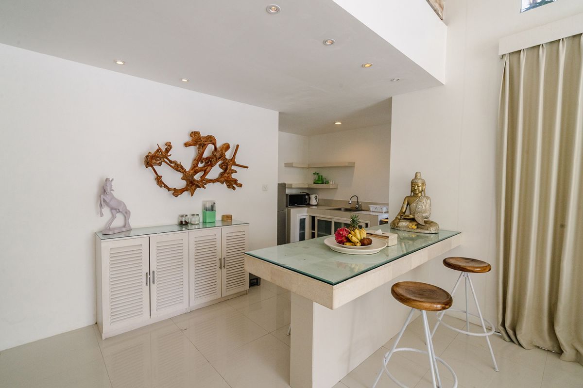 Spacious Balinese loft living room with wooden mezzanine stairs, purple sofa, TV console, white coffee table, and tropical wall art. - Bali Villas
