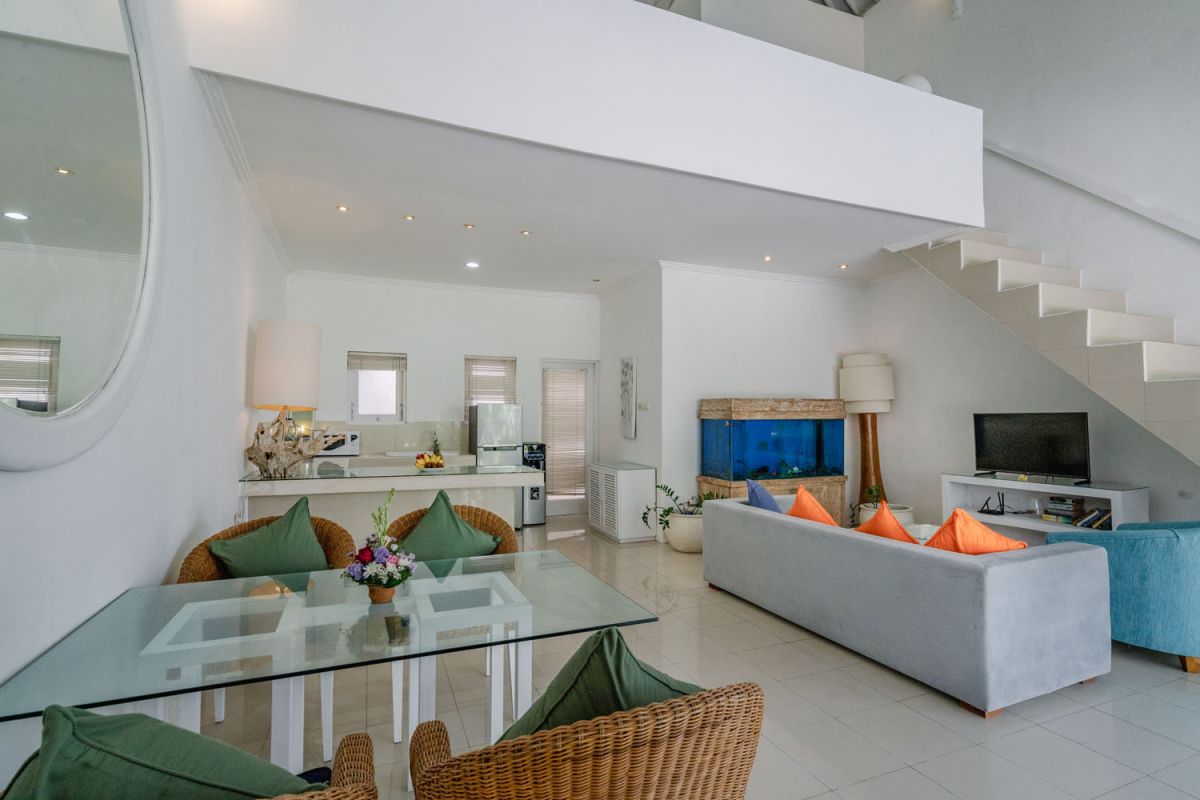 Bright tropical kitchenette with white countertops, fruit platter, louvered cabinets, fridge, and warm lamp lighting. - Bali Villas