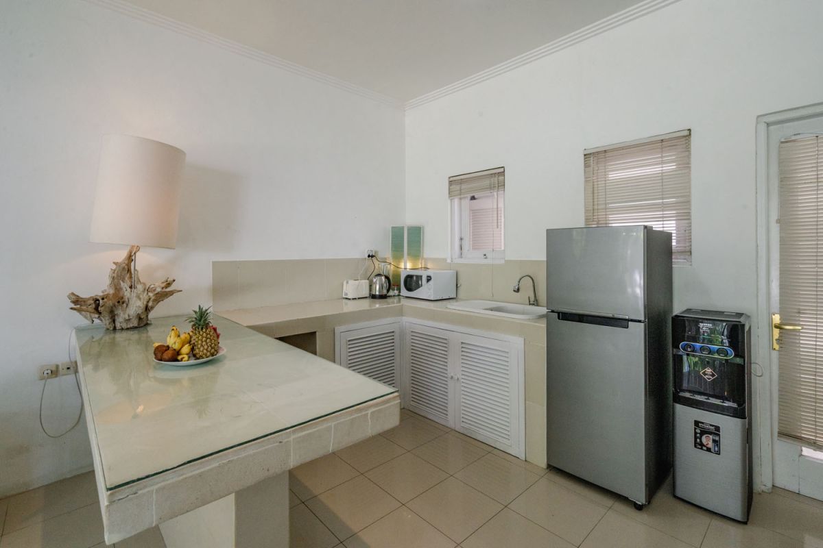 Bright tropical kitchenette with white countertops, fruit platter, louvered cabinets, fridge, and warm lamp lighting. - Bali Villas