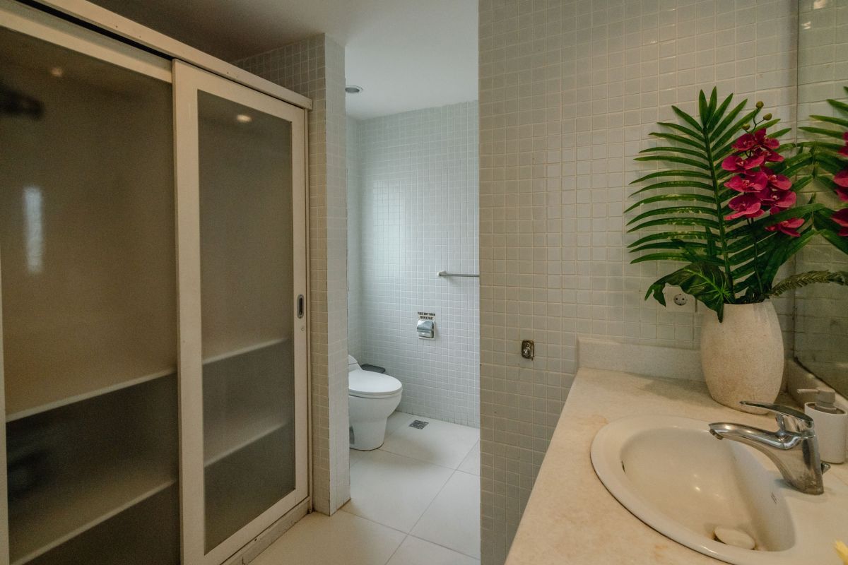 Compact modern bathroom interior with white tiled walls, toilet, sink vanity, and decorative flowers. - Bali Villas