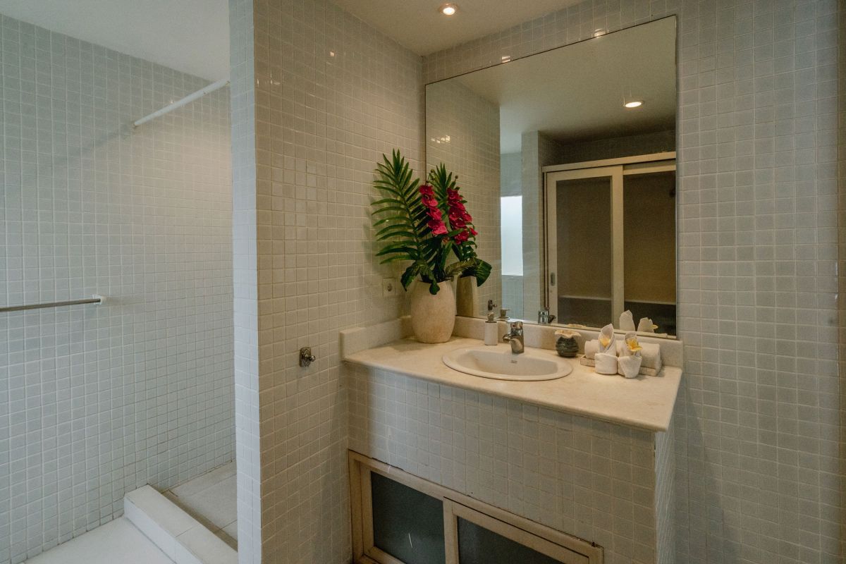 Compact modern bathroom interior with white tiled walls, toilet, sink vanity, and decorative flowers. - Bali Villas