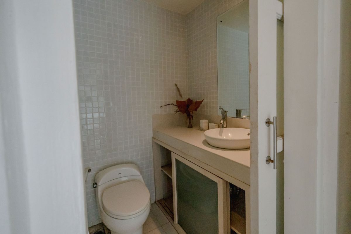 Compact modern bathroom interior with white tiled walls, toilet, sink vanity, and decorative flowers. - Bali Villas