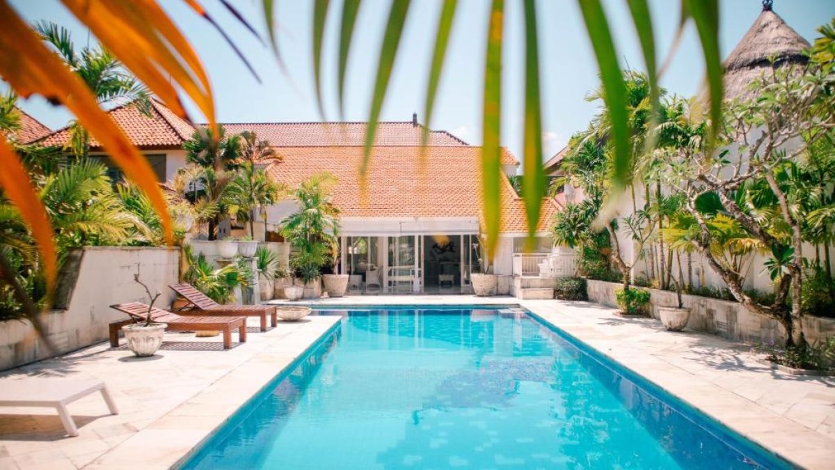 Serene Balinese villa pool with turquoise water, palm-fringed gardens, and red-tiled architecture. - Bali Villas