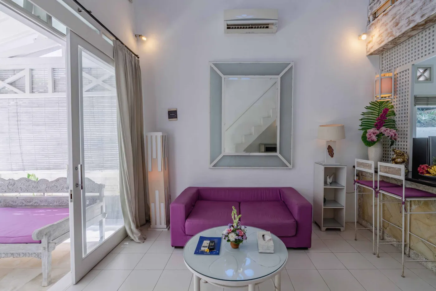 Modern bathroom interior with beige tiled walls, large frameless mirror, white vanity sink, toiletries, and walk-in shower. - Bali Villas