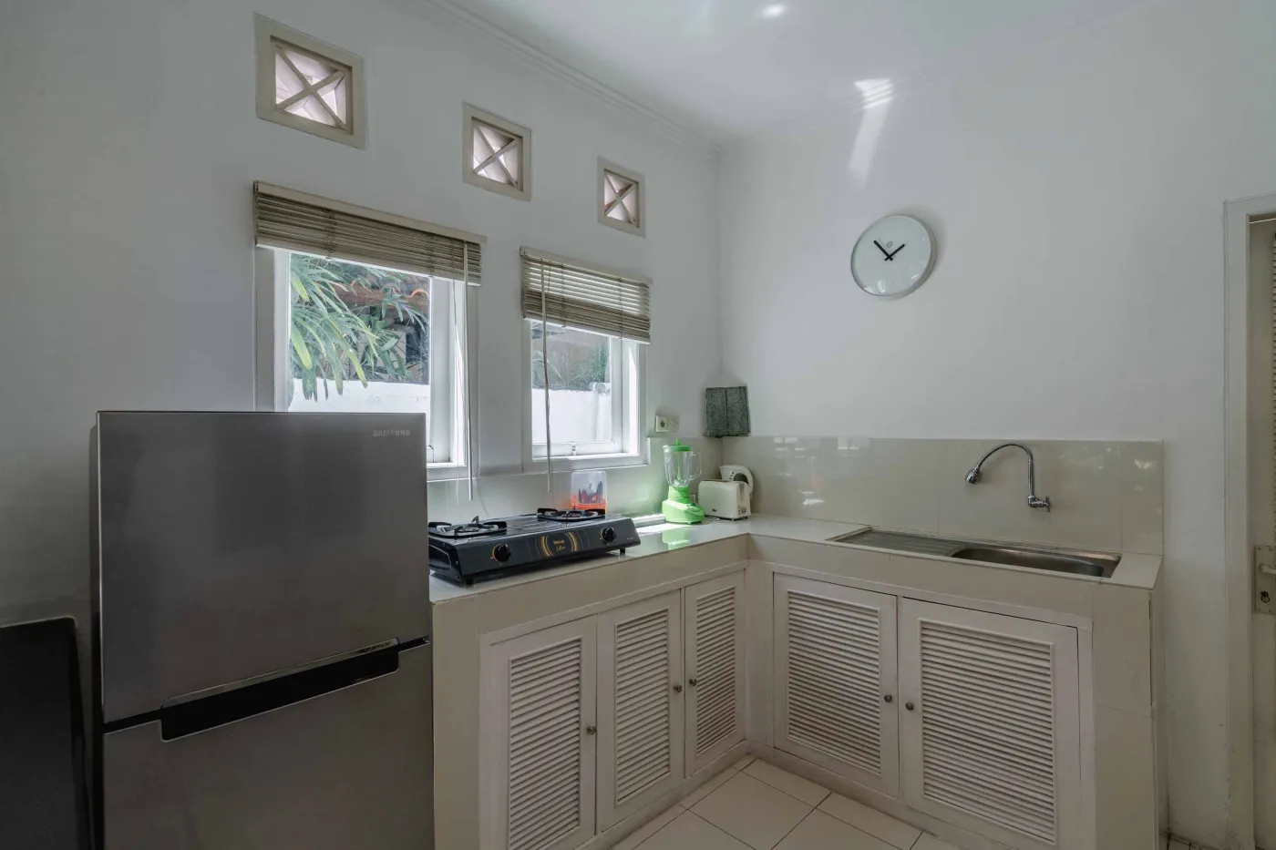 Modern bathroom interior with beige tiled walls, large frameless mirror, white vanity sink, toiletries, and walk-in shower. - Bali Villas
