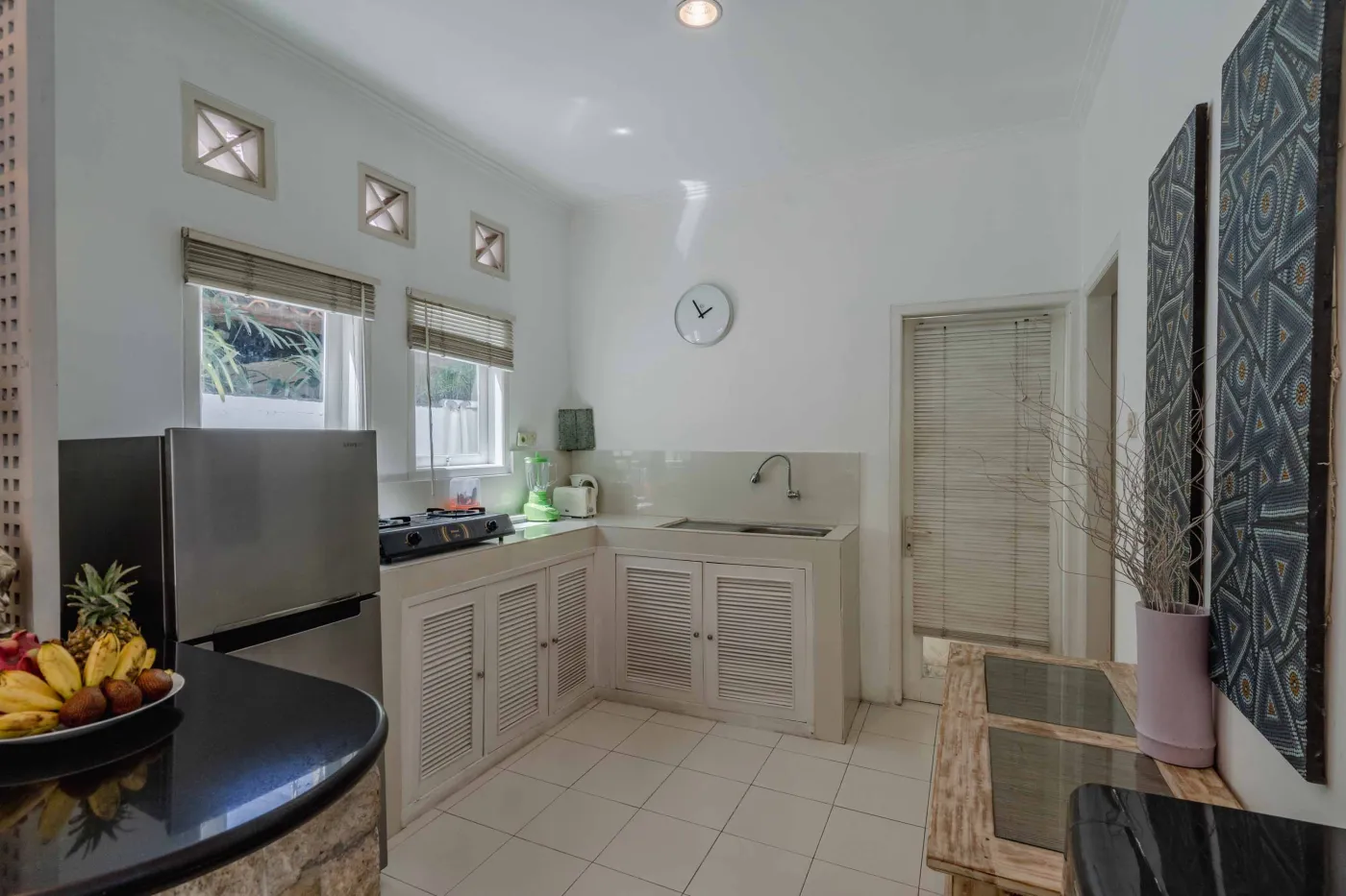 Modern bathroom interior with beige tiled walls, large frameless mirror, white vanity sink, toiletries, and walk-in shower. - Bali Villas