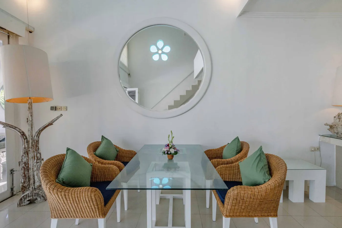 Modern open-plan tropical interior with sliding glass doors connecting living room to outdoor seating area, white tiled floors, plush sofas, and potted plants. - Bali Villas