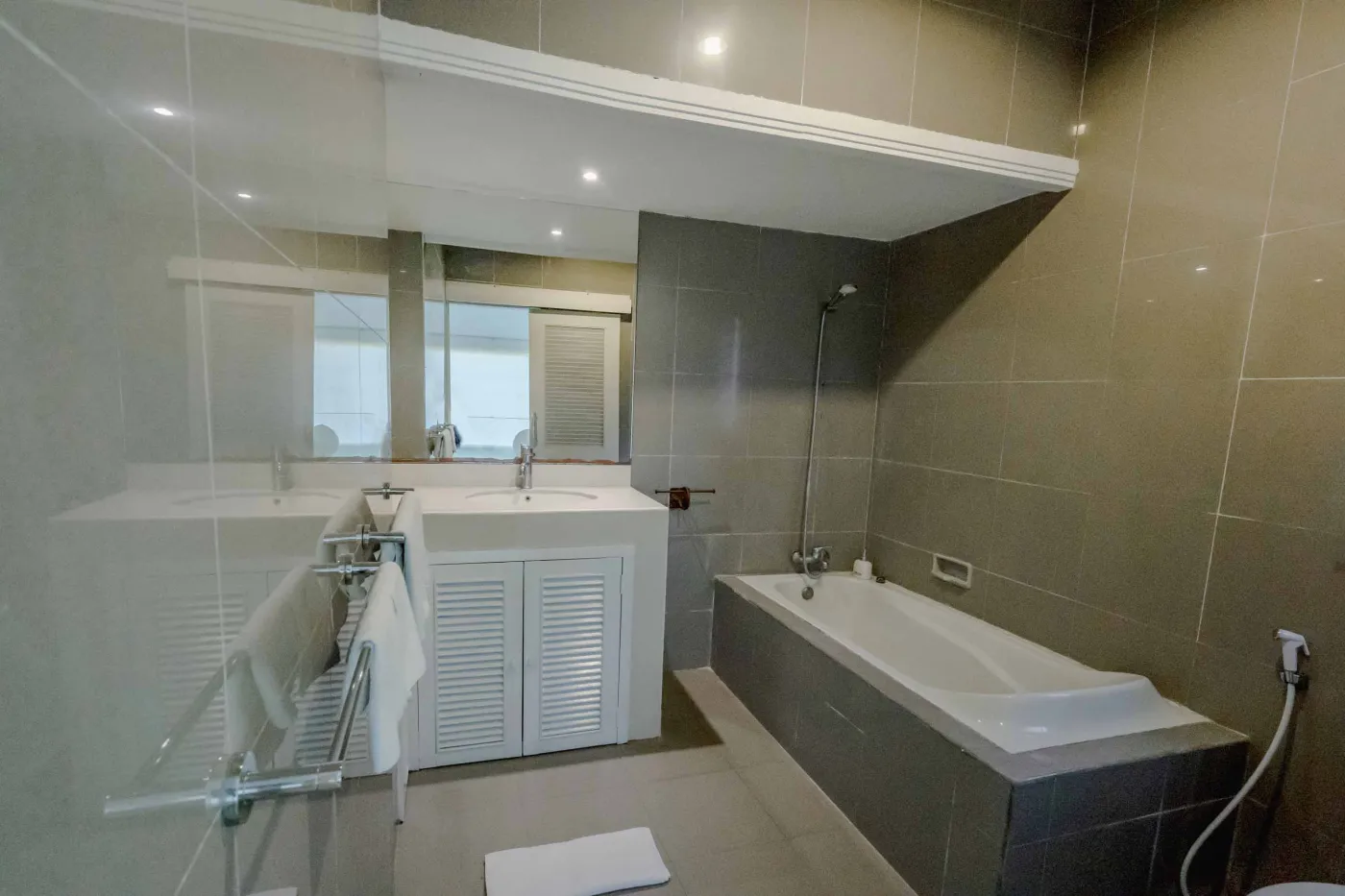 Modern open-plan tropical interior with sliding glass doors connecting living room to outdoor seating area, white tiled floors, plush sofas, and potted plants. - Bali Villas