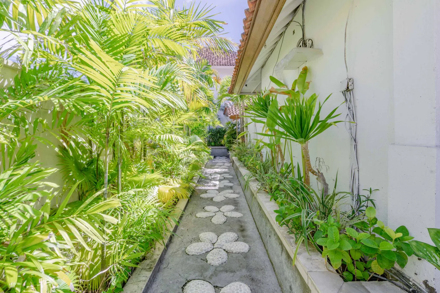 Modern open-plan tropical interior with sliding glass doors connecting living room to outdoor seating area, white tiled floors, plush sofas, and potted plants. - Bali Villas
