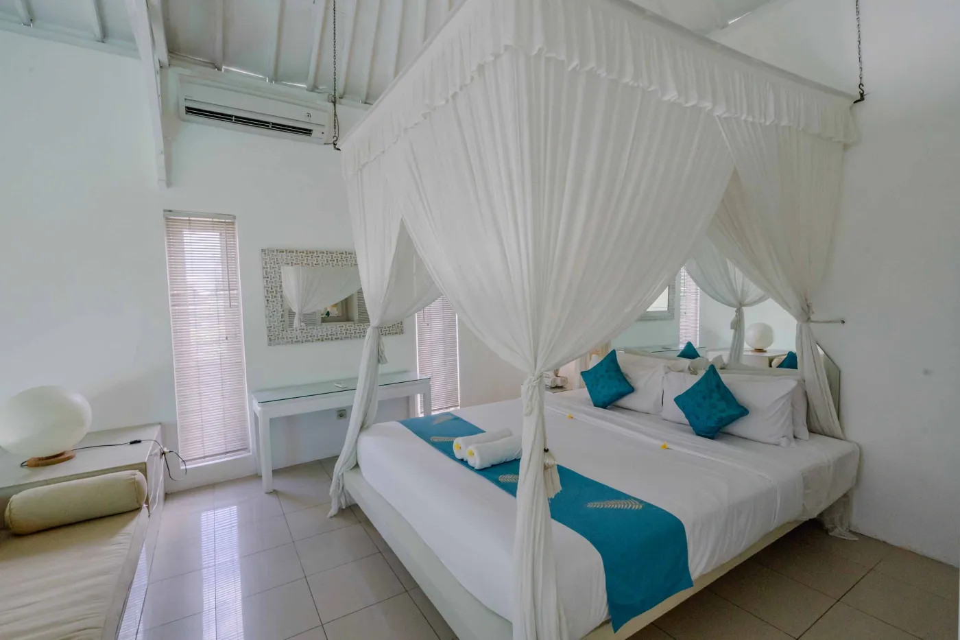 Modern open-plan tropical interior with sliding glass doors connecting living room to outdoor seating area, white tiled floors, plush sofas, and potted plants. - Bali Villas