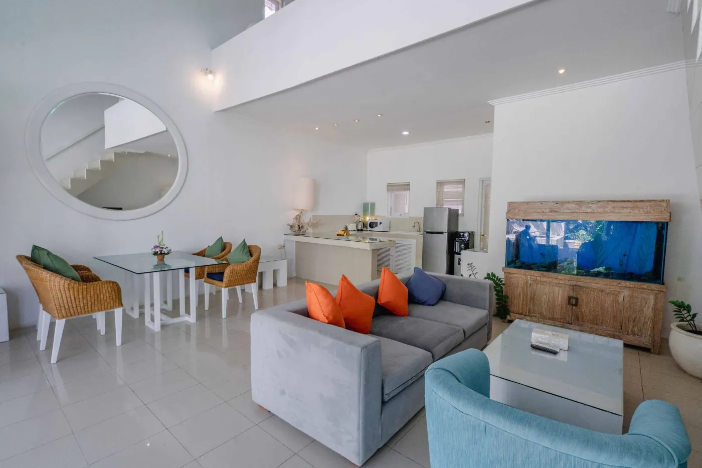 Modern open-plan tropical interior with sliding glass doors connecting living room to outdoor seating area, white tiled floors, plush sofas, and potted plants. - Bali Villas