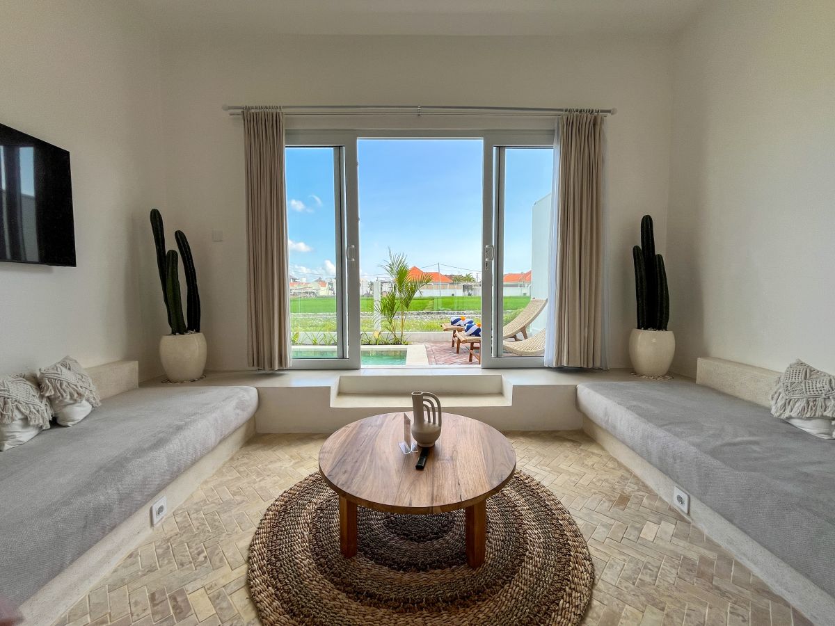 Elegant Bali villa dining room with wooden table set for meal, rattan chairs, and tropical pool view through glass doors. - Bali Villas