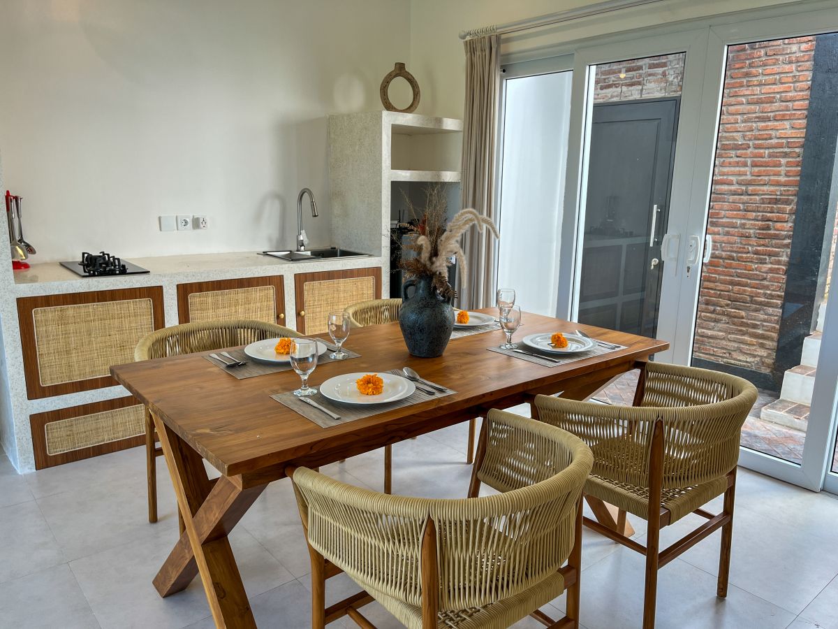 Elegant Bali villa dining room with wooden table set for meal, rattan chairs, and tropical pool view through glass doors. - Bali Villas