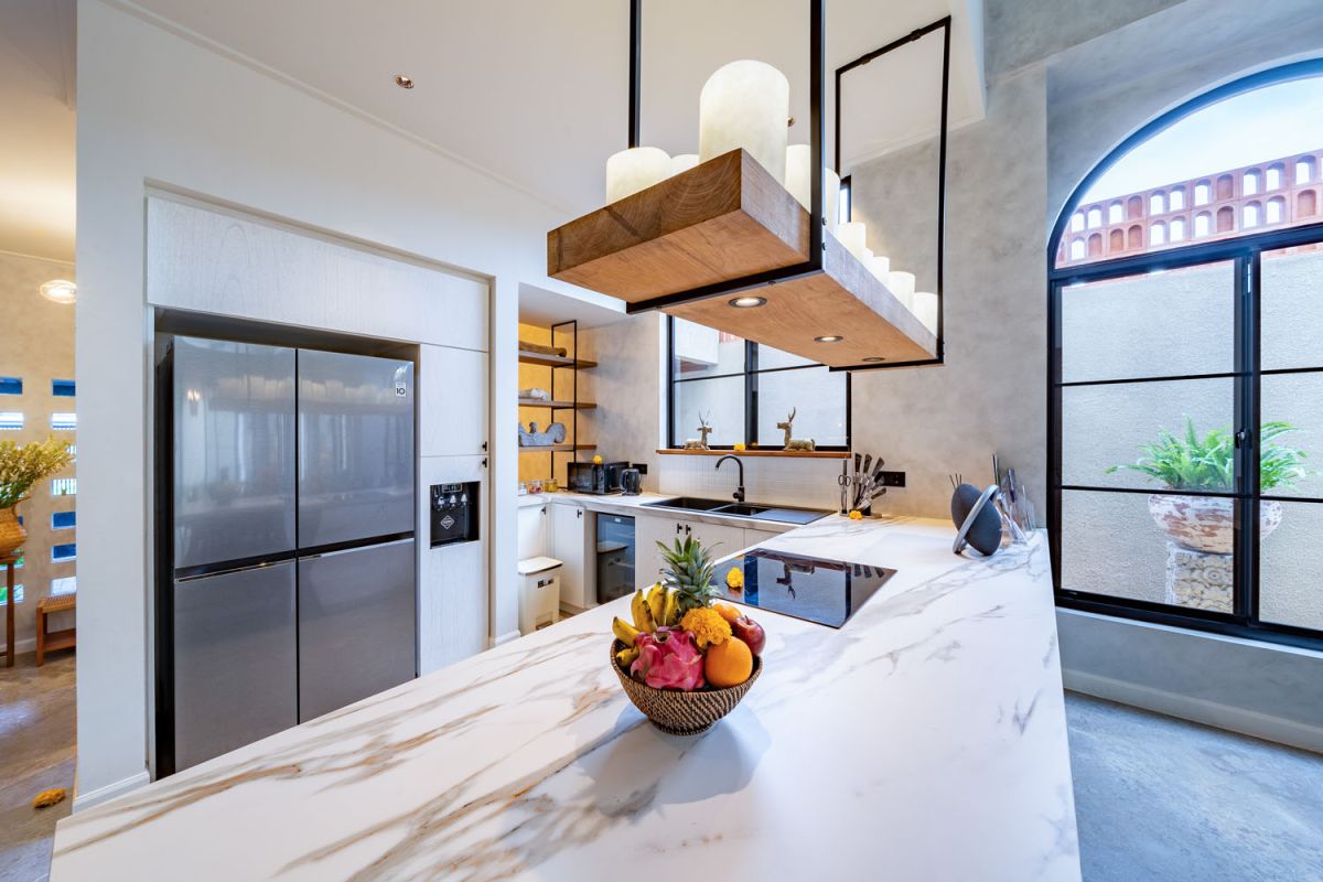 Modern luxury bathroom featuring white marble walls, wooden vanity sink, arched mirror, tropical red flower arrangement, and glass-enclosed shower. - Bali Villas