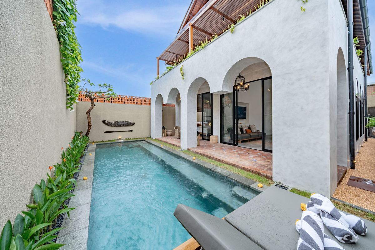 Modern luxury bathroom featuring white marble walls, wooden vanity sink, arched mirror, tropical red flower arrangement, and glass-enclosed shower. - Bali Villas