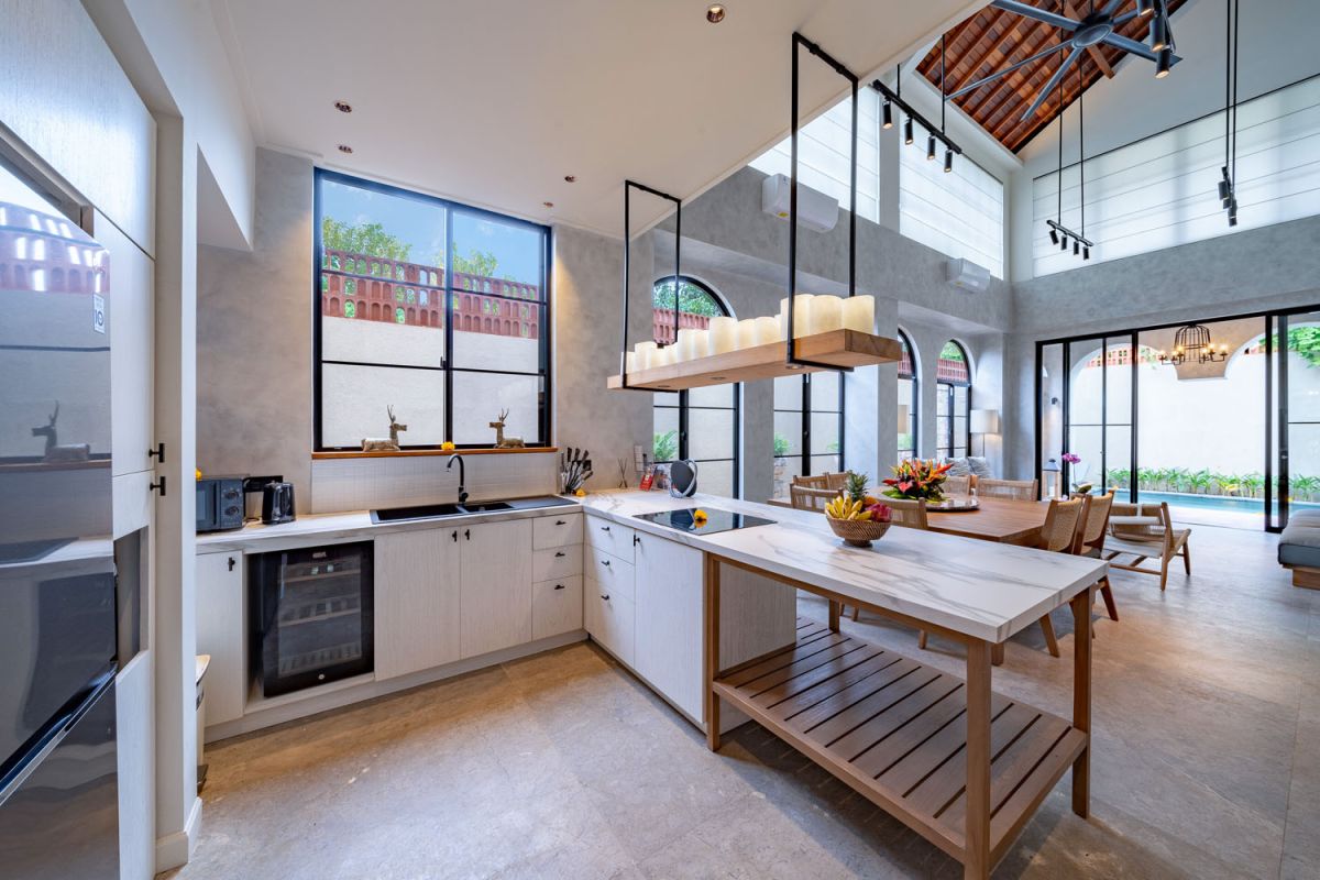 Modern luxury bathroom featuring white marble walls, wooden vanity sink, arched mirror, tropical red flower arrangement, and glass-enclosed shower. - Bali Villas