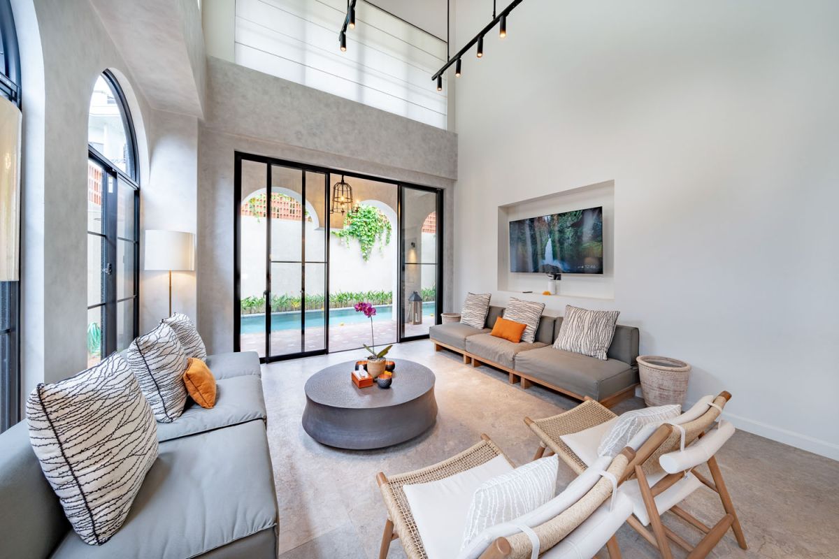 Modern luxury bathroom featuring white marble walls, wooden vanity sink, arched mirror, tropical red flower arrangement, and glass-enclosed shower. - Bali Villas