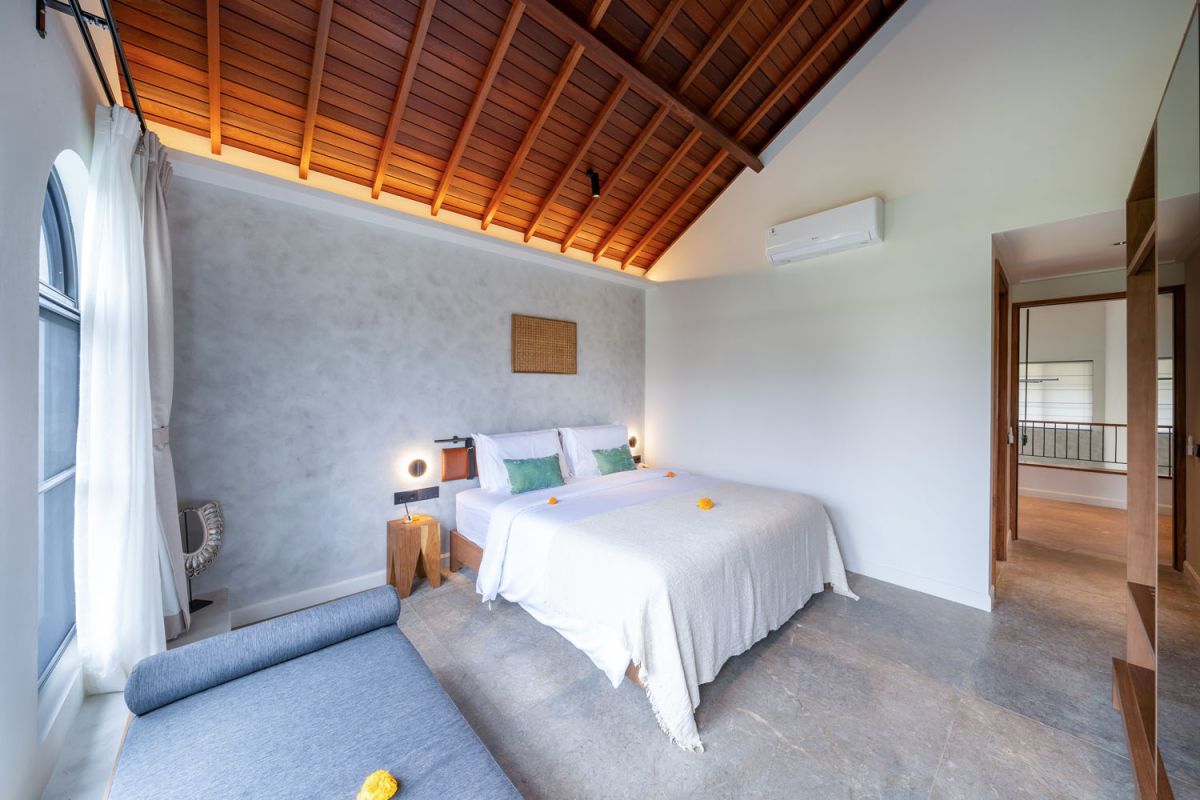 Modern luxury bathroom featuring white marble walls, wooden vanity sink, arched mirror, tropical red flower arrangement, and glass-enclosed shower. - Bali Villas