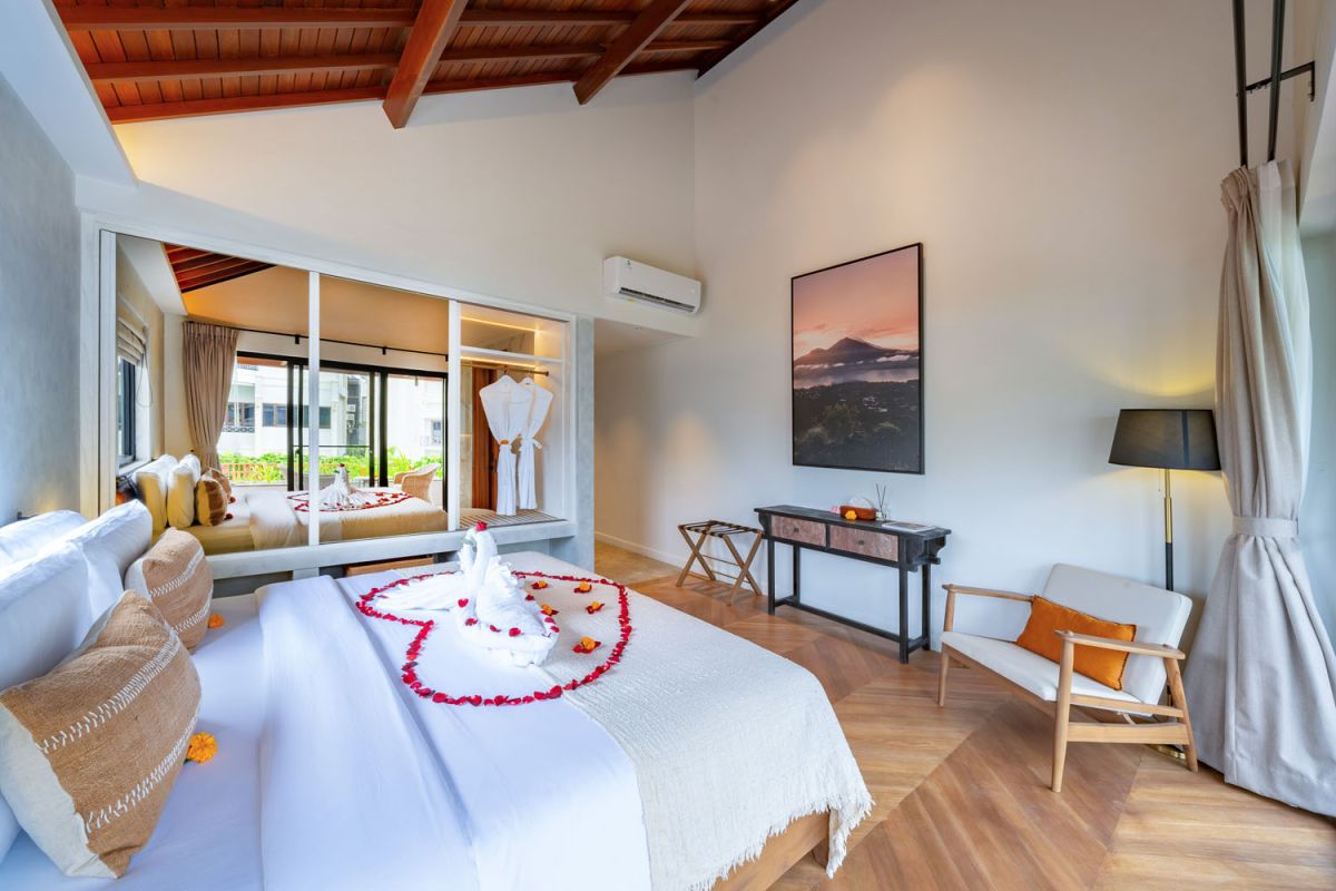 Modern luxury bathroom featuring white marble walls, wooden vanity sink, arched mirror, tropical red flower arrangement, and glass-enclosed shower. - Bali Villas