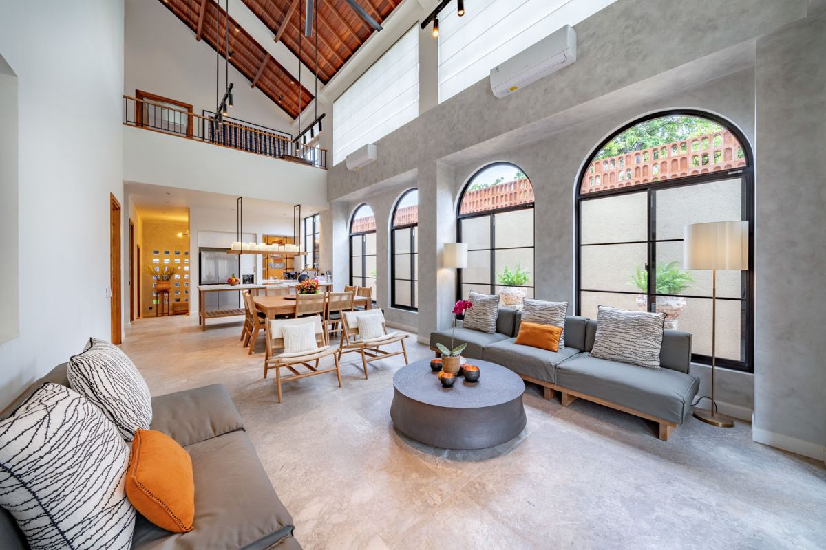 Modern luxury bathroom featuring white marble walls, wooden vanity sink, arched mirror, tropical red flower arrangement, and glass-enclosed shower. - Bali Villas