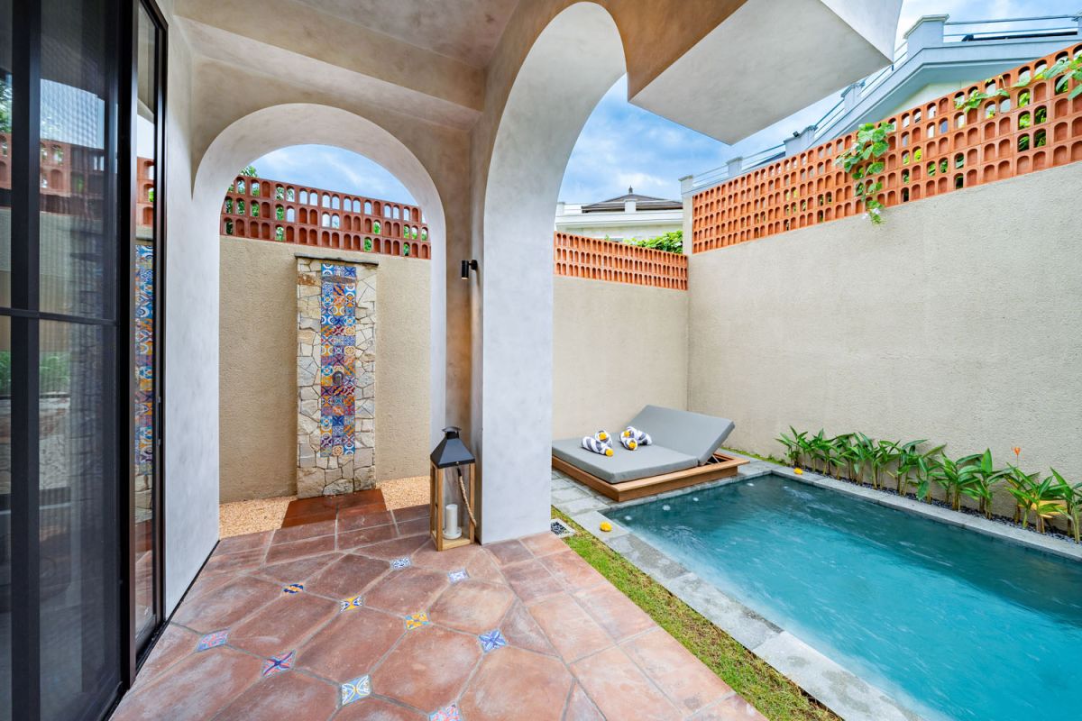 Modern luxury bathroom featuring white marble walls, wooden vanity sink, arched mirror, tropical red flower arrangement, and glass-enclosed shower. - Bali Villas