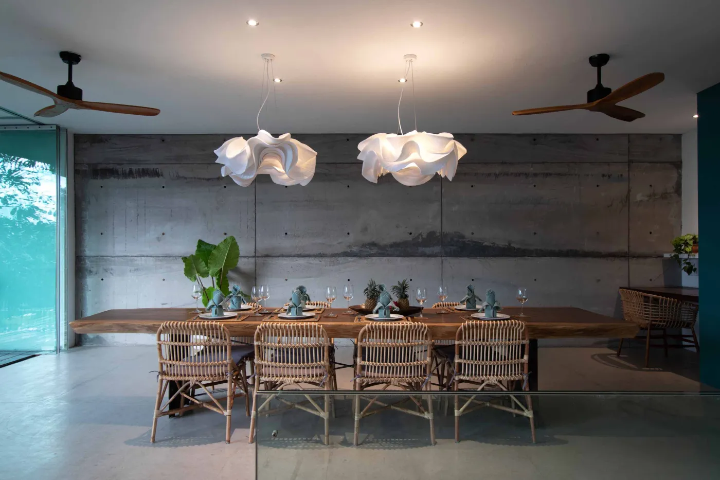 Cozy outdoor balcony lounge with white armchairs, blue tiled table, and potted plants, overlooking tropical palm trees at dusk sunset. - Bali Villas
