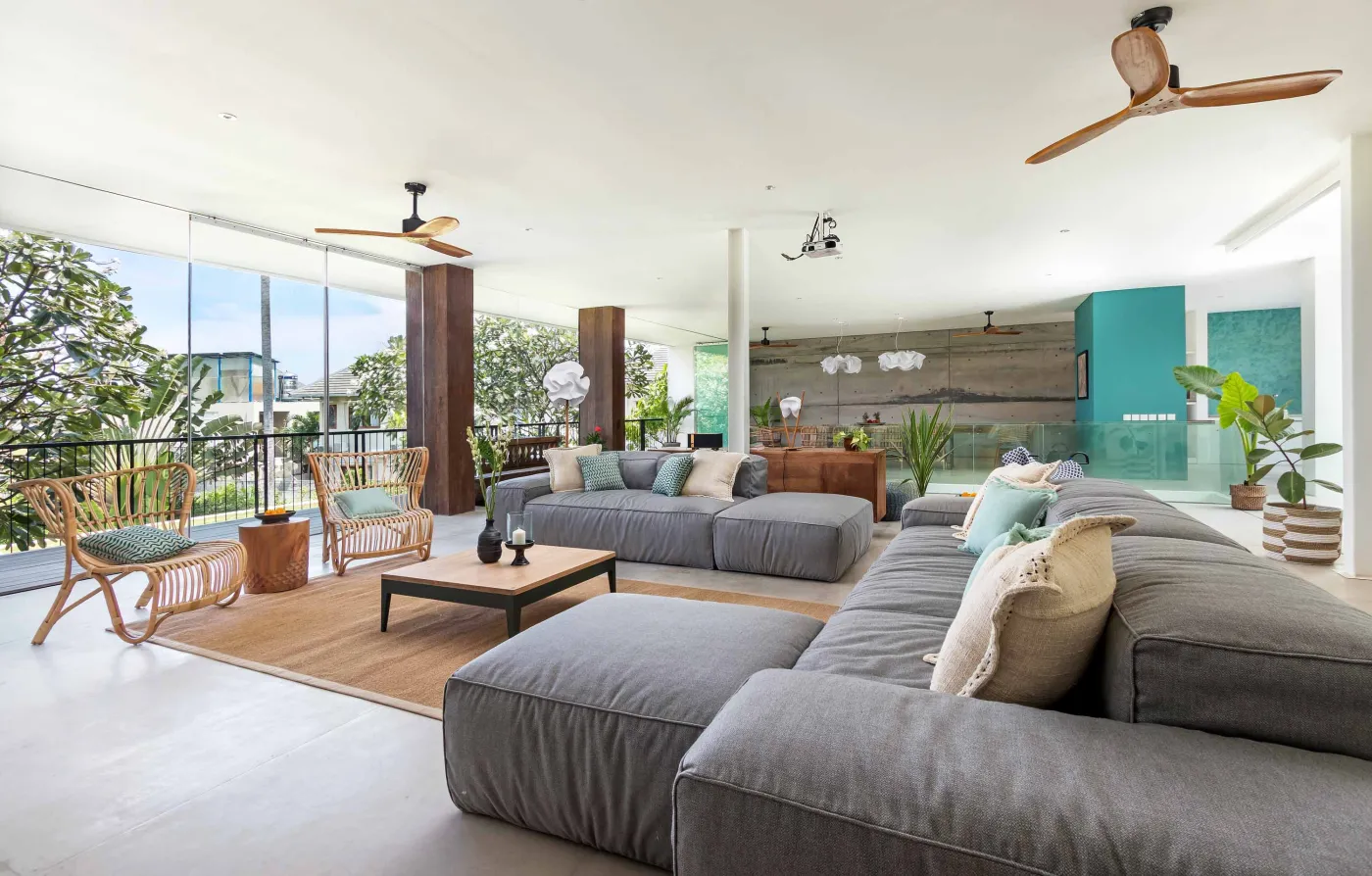 Cozy outdoor balcony lounge with white armchairs, blue tiled table, and potted plants, overlooking tropical palm trees at dusk sunset. - Bali Villas