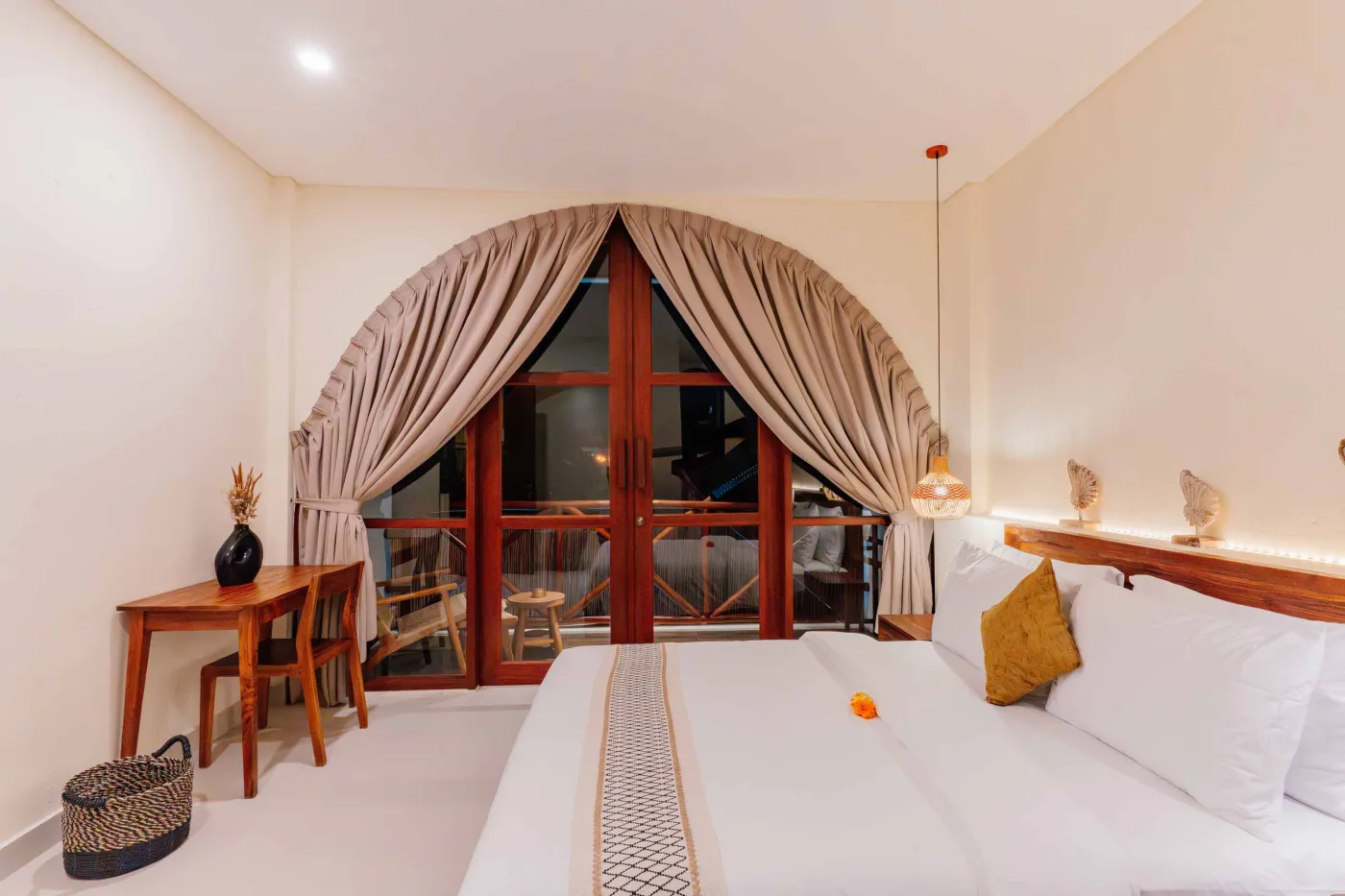 Luxurious spa bathroom with white freestanding bathtub filled with floating red hibiscus petals, wooden mirror, and brass fixtures in soft natural light. - Bali Villas