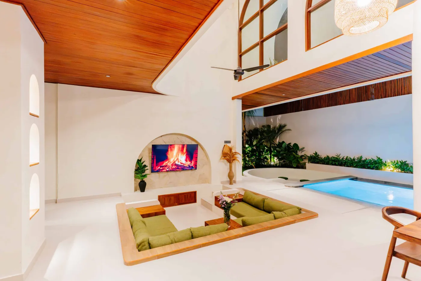 Luxurious spa bathroom with white freestanding bathtub filled with floating red hibiscus petals, wooden mirror, and brass fixtures in soft natural light. - Bali Villas
