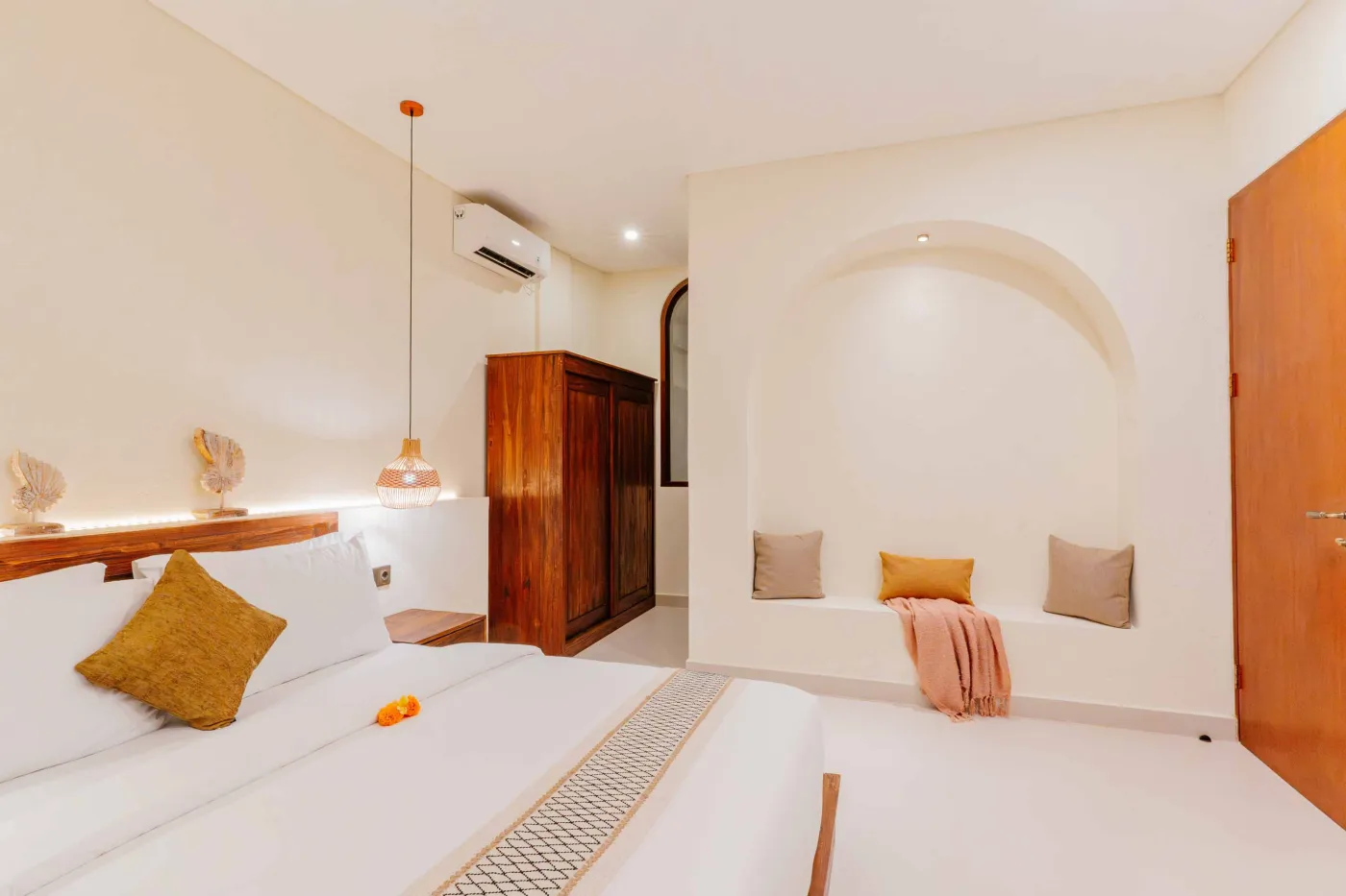 Luxurious spa bathroom with white freestanding bathtub filled with floating red hibiscus petals, wooden mirror, and brass fixtures in soft natural light. - Bali Villas