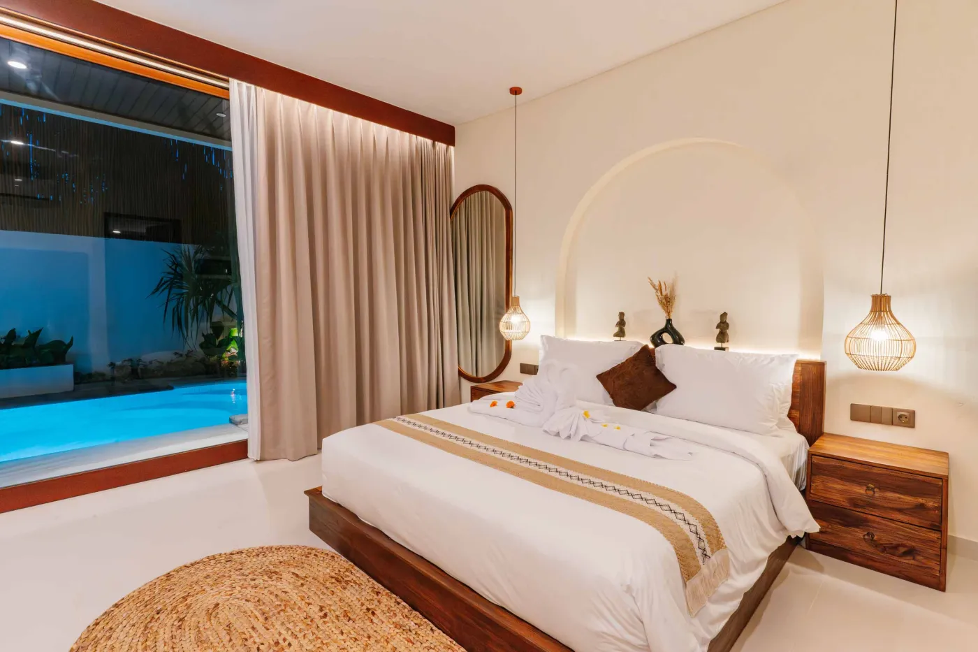 Luxurious spa bathroom with white freestanding bathtub filled with floating red hibiscus petals, wooden mirror, and brass fixtures in soft natural light. - Bali Villas