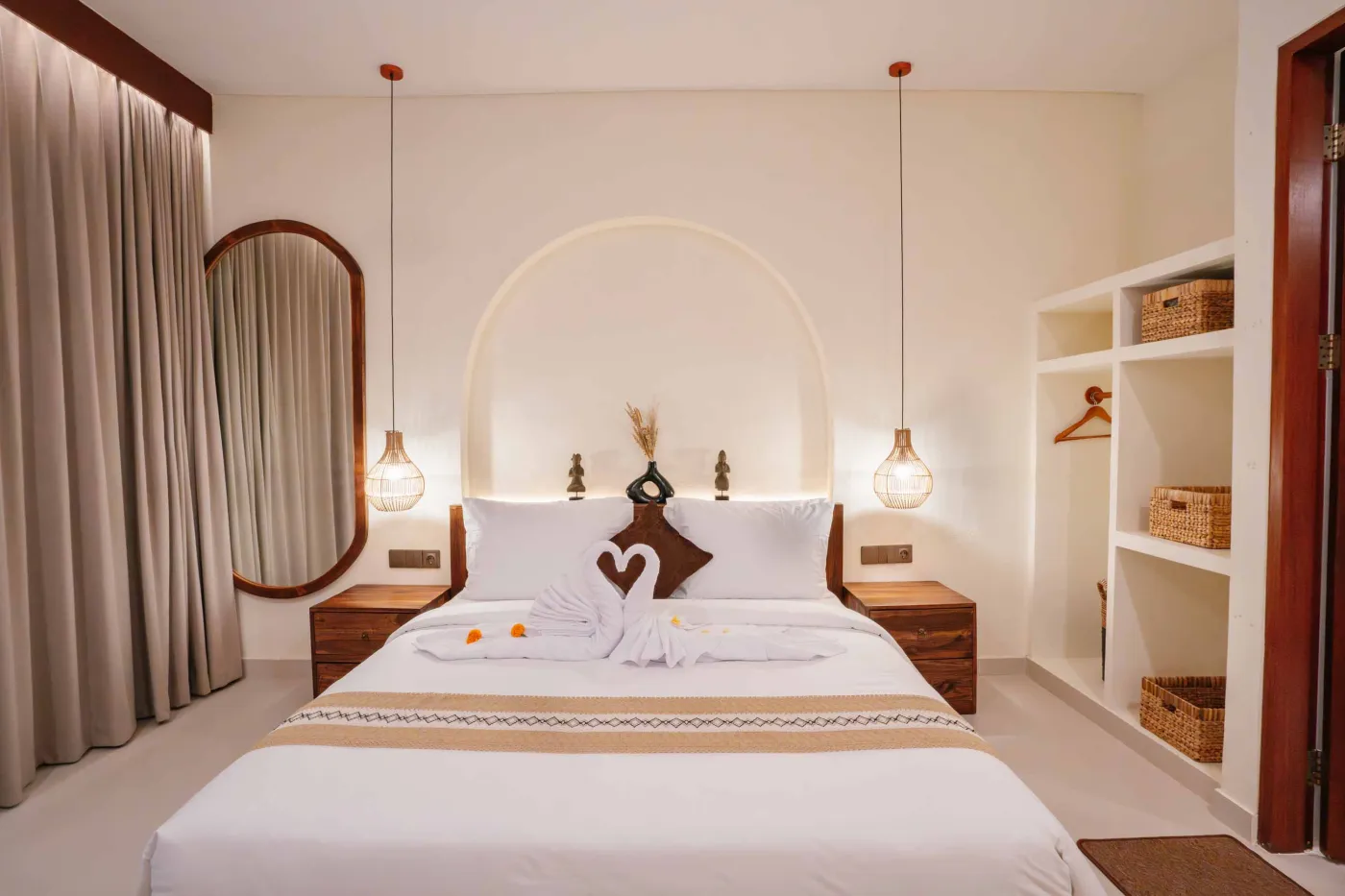 Luxurious spa bathroom with white freestanding bathtub filled with floating red hibiscus petals, wooden mirror, and brass fixtures in soft natural light. - Bali Villas