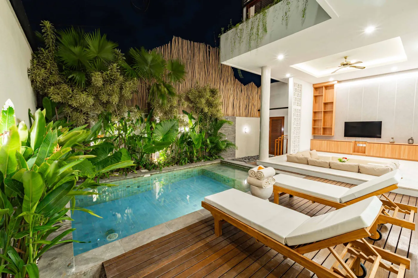 Luxury tropical villa with infinity pool, lounge chairs, and lush greenery under night lighting. - Bali Villas