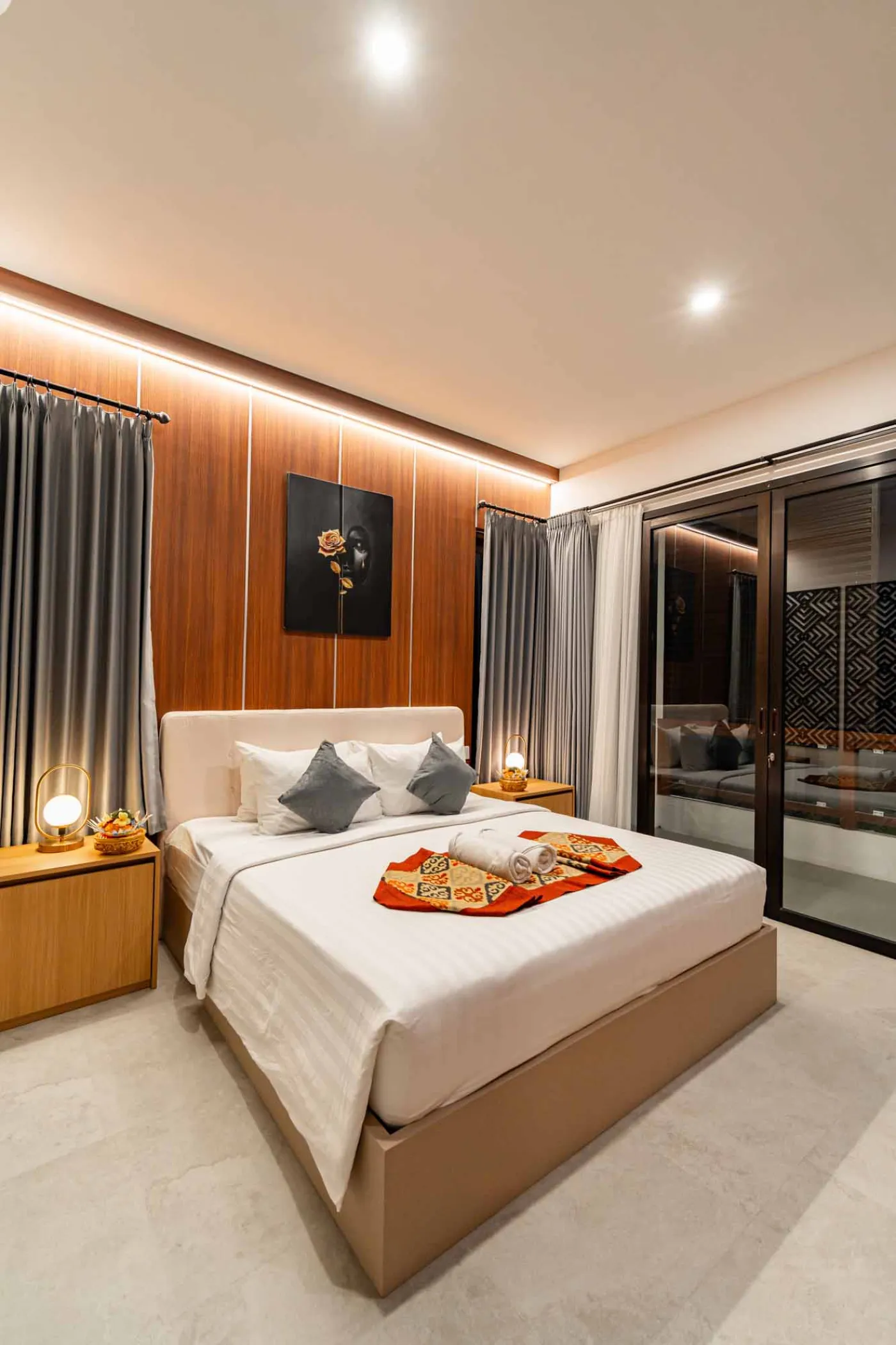 Modern bathroom with round wooden-framed mirror, white vessel sink on black countertop, toilet, and glass shower enclosure. - Bali Villas
