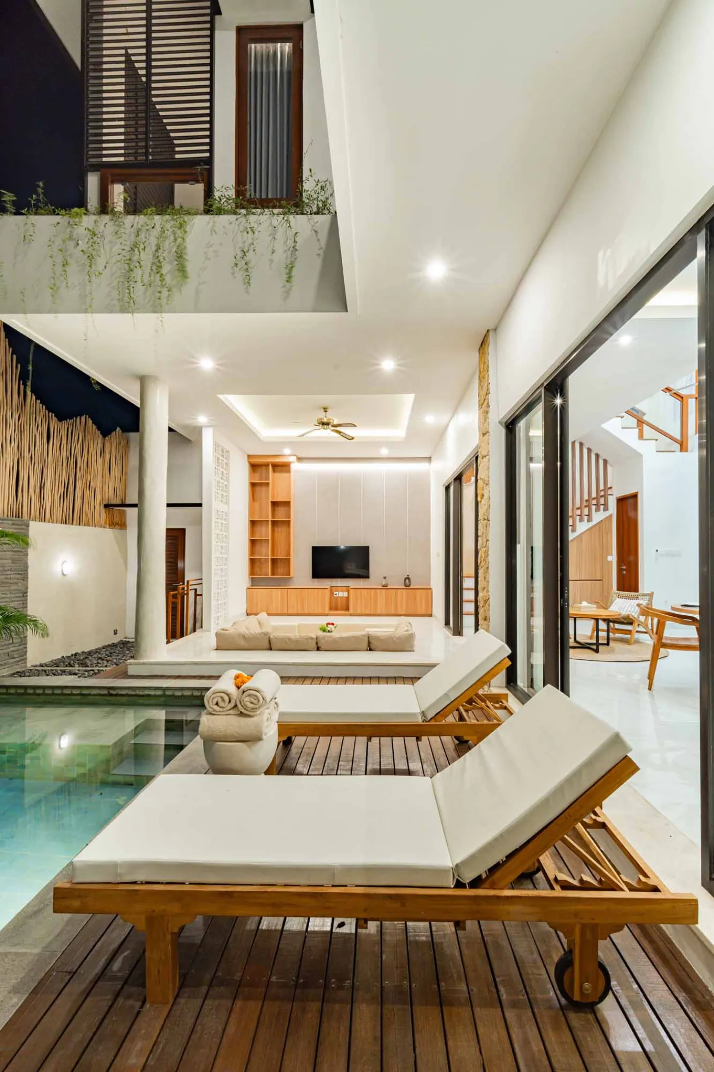 Modern bathroom with round wooden-framed mirror, white vessel sink on black countertop, toilet, and glass shower enclosure. - Bali Villas