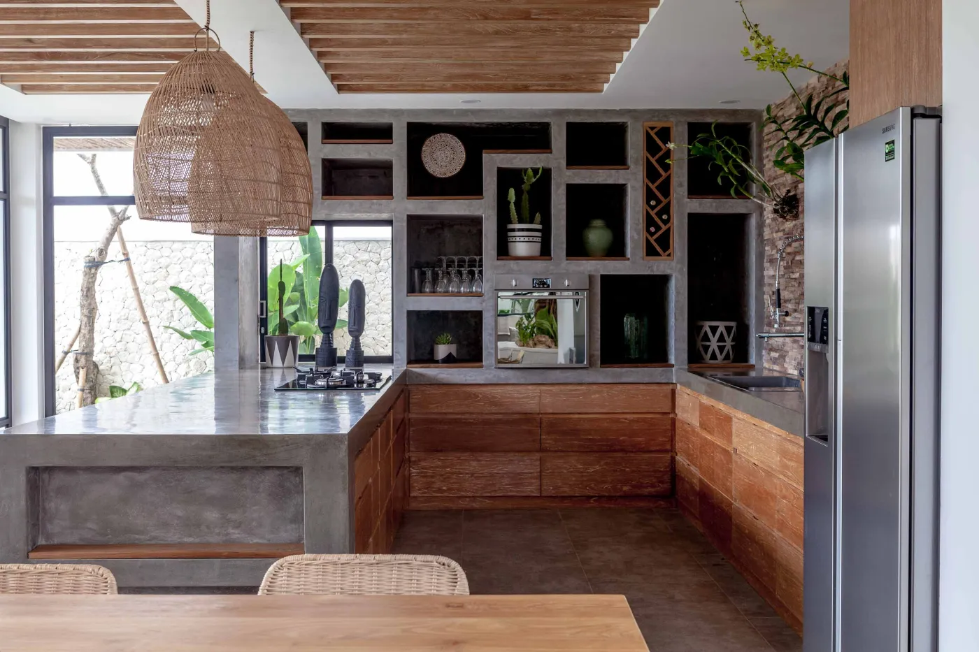 Spacious modern tropical kitchen and dining room with wooden table, rattan chairs, pendant lights, indoor plants, and large windows. - Bali Villas