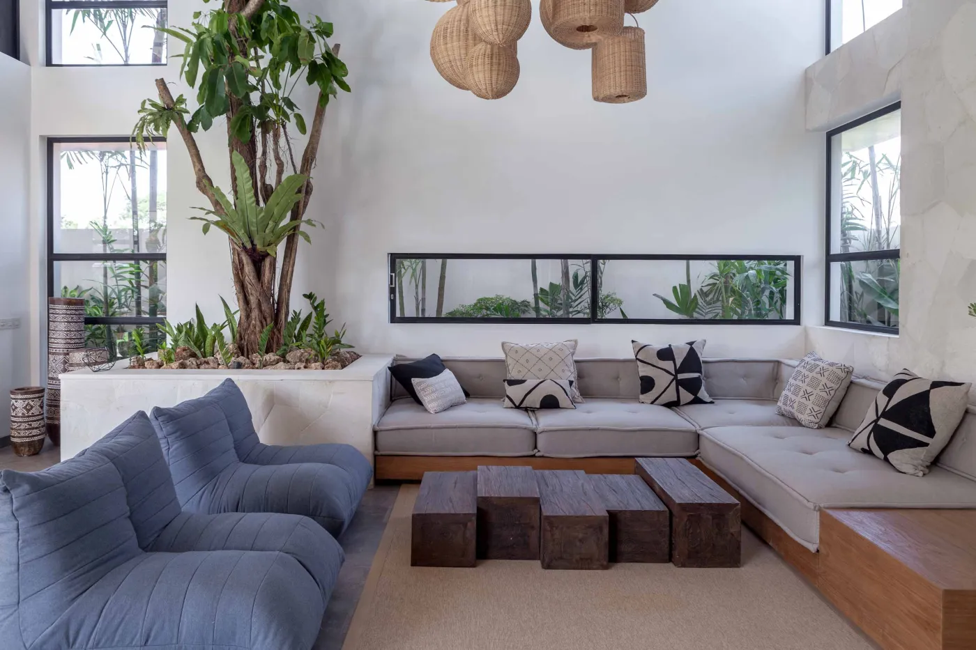 Spacious modern tropical kitchen and dining room with wooden table, rattan chairs, pendant lights, indoor plants, and large windows. - Bali Villas