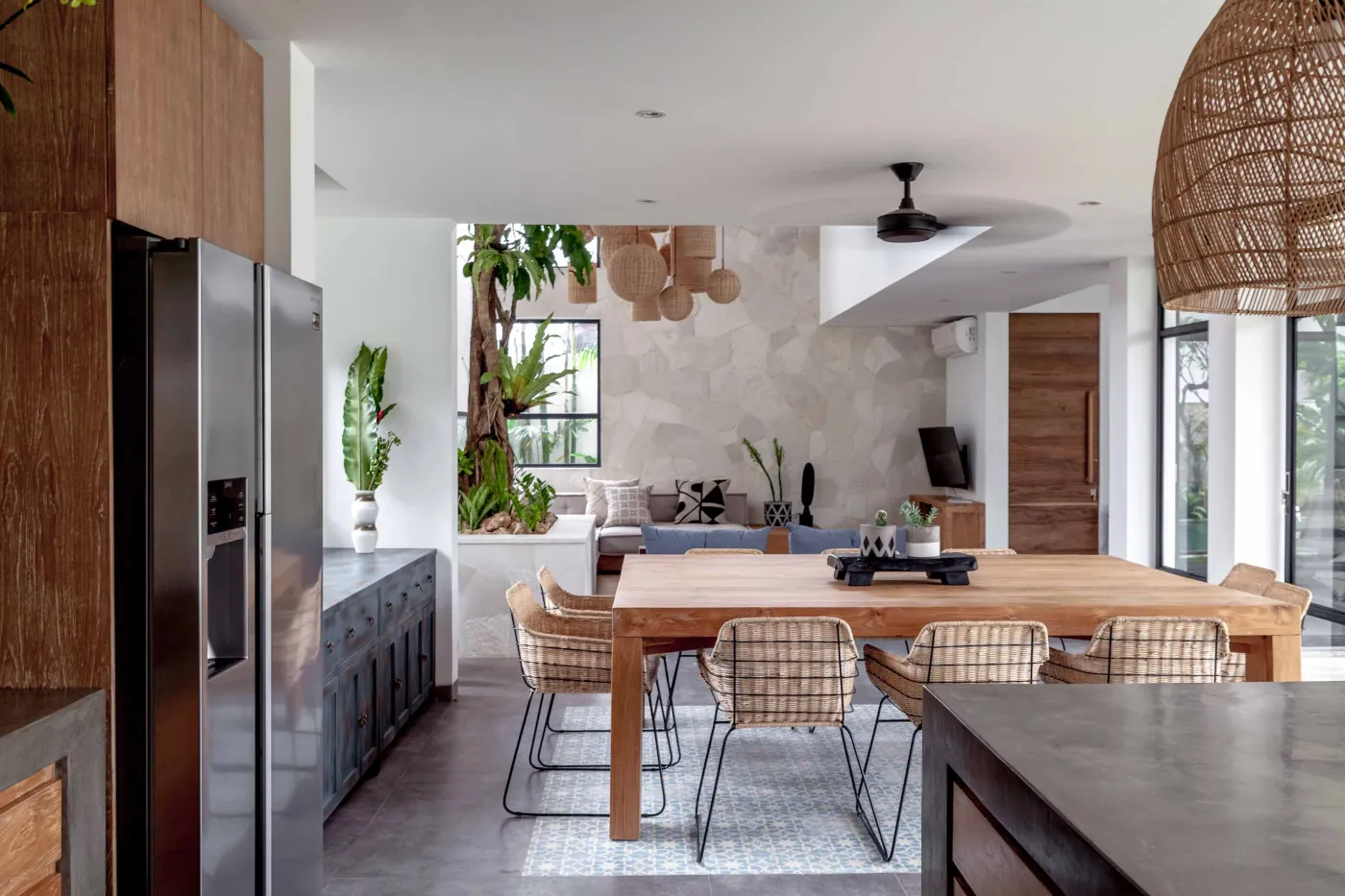 Spacious modern tropical kitchen and dining room with wooden table, rattan chairs, pendant lights, indoor plants, and large windows. - Bali Villas