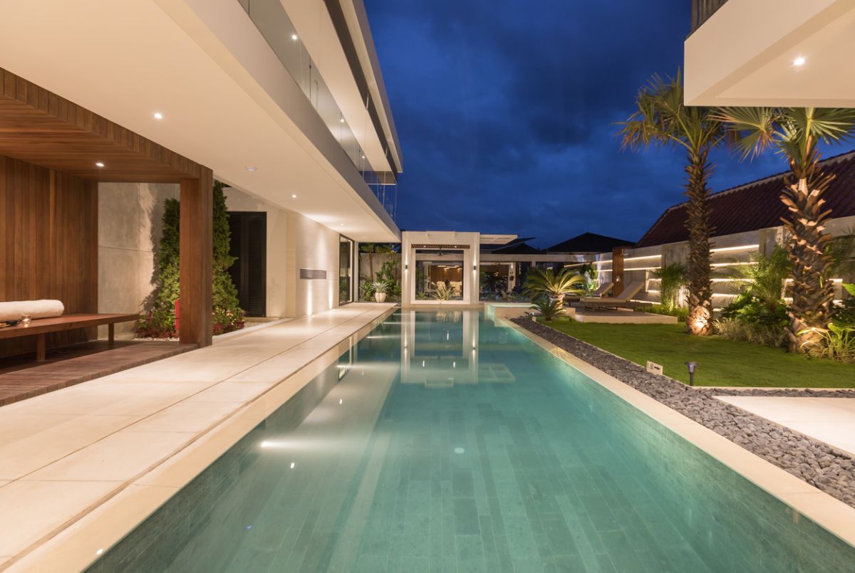 Elegant outdoor dining table set for dinner in a luxurious Bali villa, with tropical plants, pool view, and NVYL branding at night. - Bali Villas