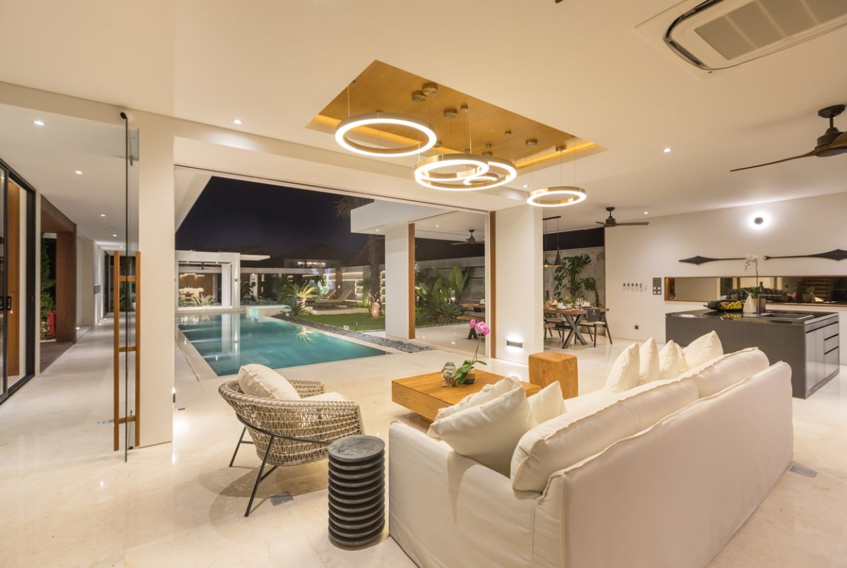 Elegant outdoor dining table set for dinner in a luxurious Bali villa, with tropical plants, pool view, and NVYL branding at night. - Bali Villas