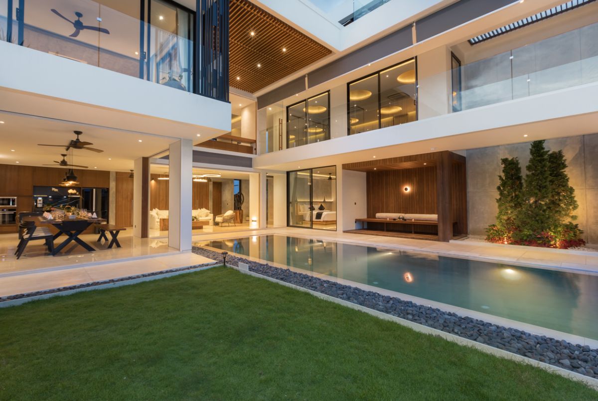 Elegant outdoor dining table set for dinner in a luxurious Bali villa, with tropical plants, pool view, and NVYL branding at night. - Bali Villas