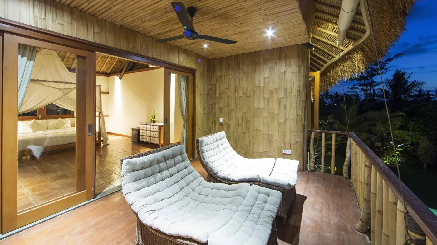 Spacious open-plan Bali villa living area with white sofas, rustic wooden coffee table, bamboo ceiling, tropical plants, and Buddha statue. - Bali Villas